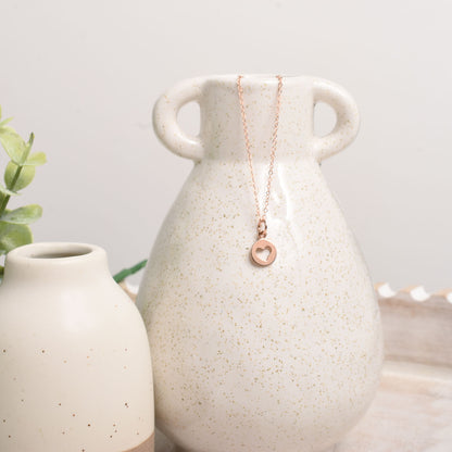 Necklace with a heart pendant draped over a ceramic vase on a light background