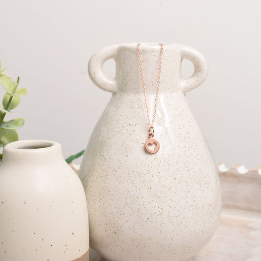 Necklace with a heart pendant draped over a ceramic vase on a light background