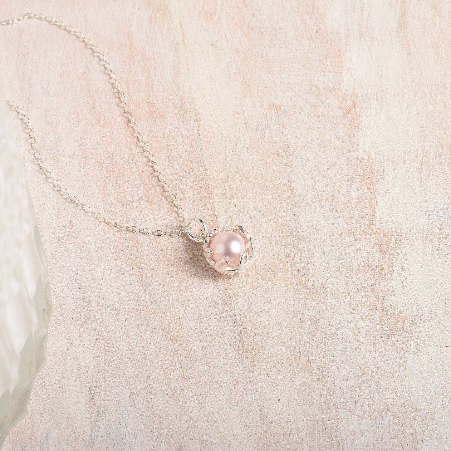 Necklace with a pink pearl pendant on a wood background