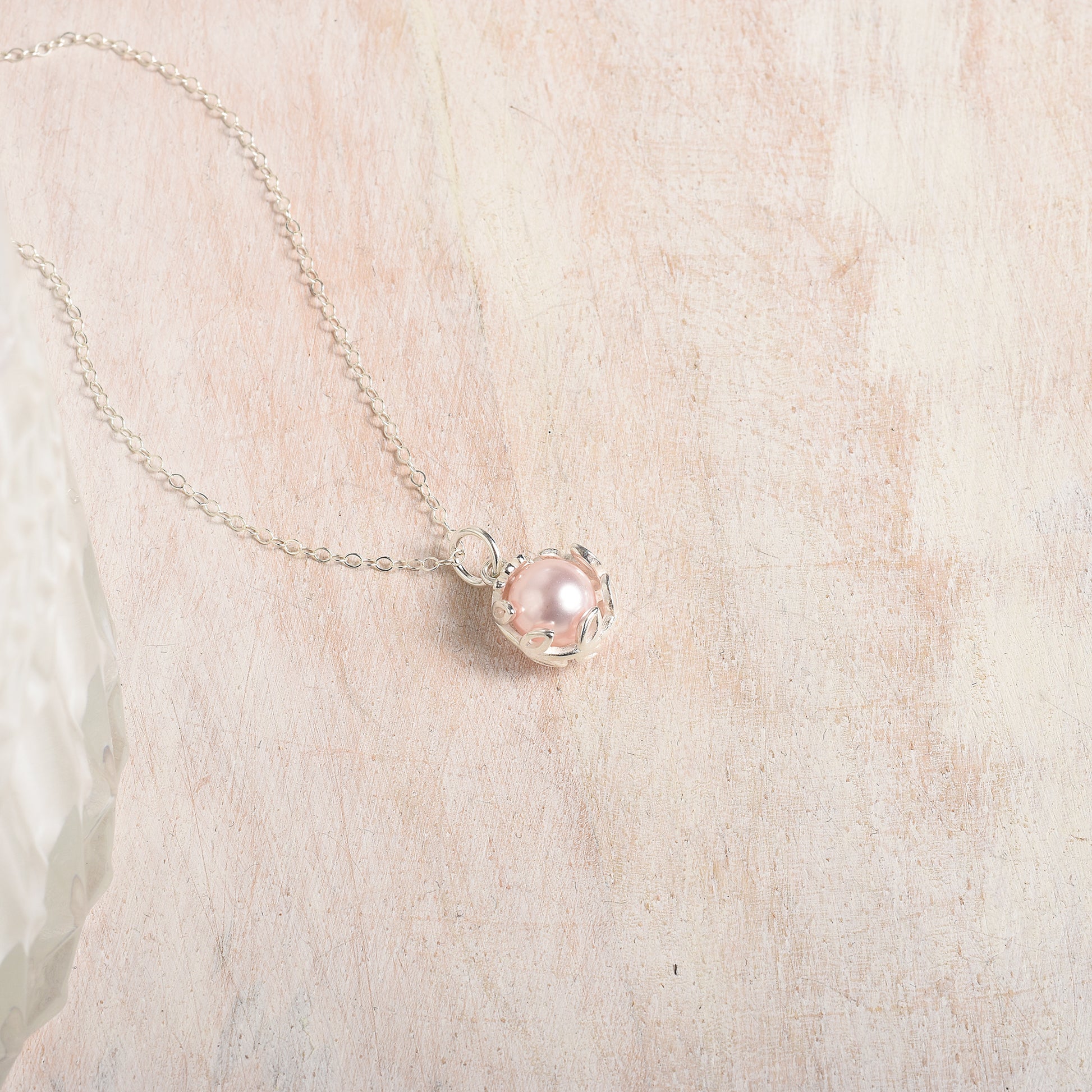 Necklace with a pink pearl pendant on a wood background