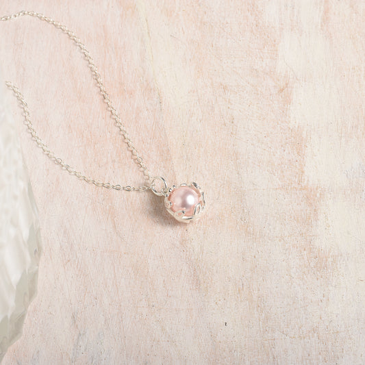 Necklace with a pink pearl pendant on a wood background
