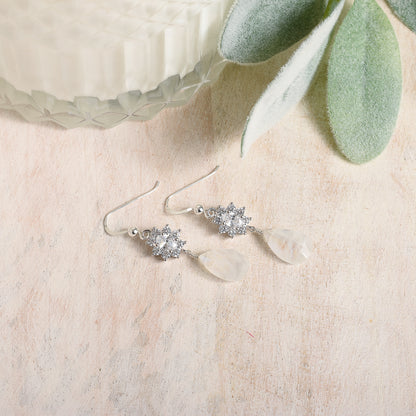 Silver earrings with CZ stones and moonstone on a light wooden surface with green leaves.