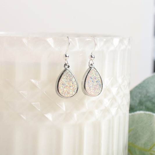 Teardrop-shaped silver earrings with glittery finish on a white background