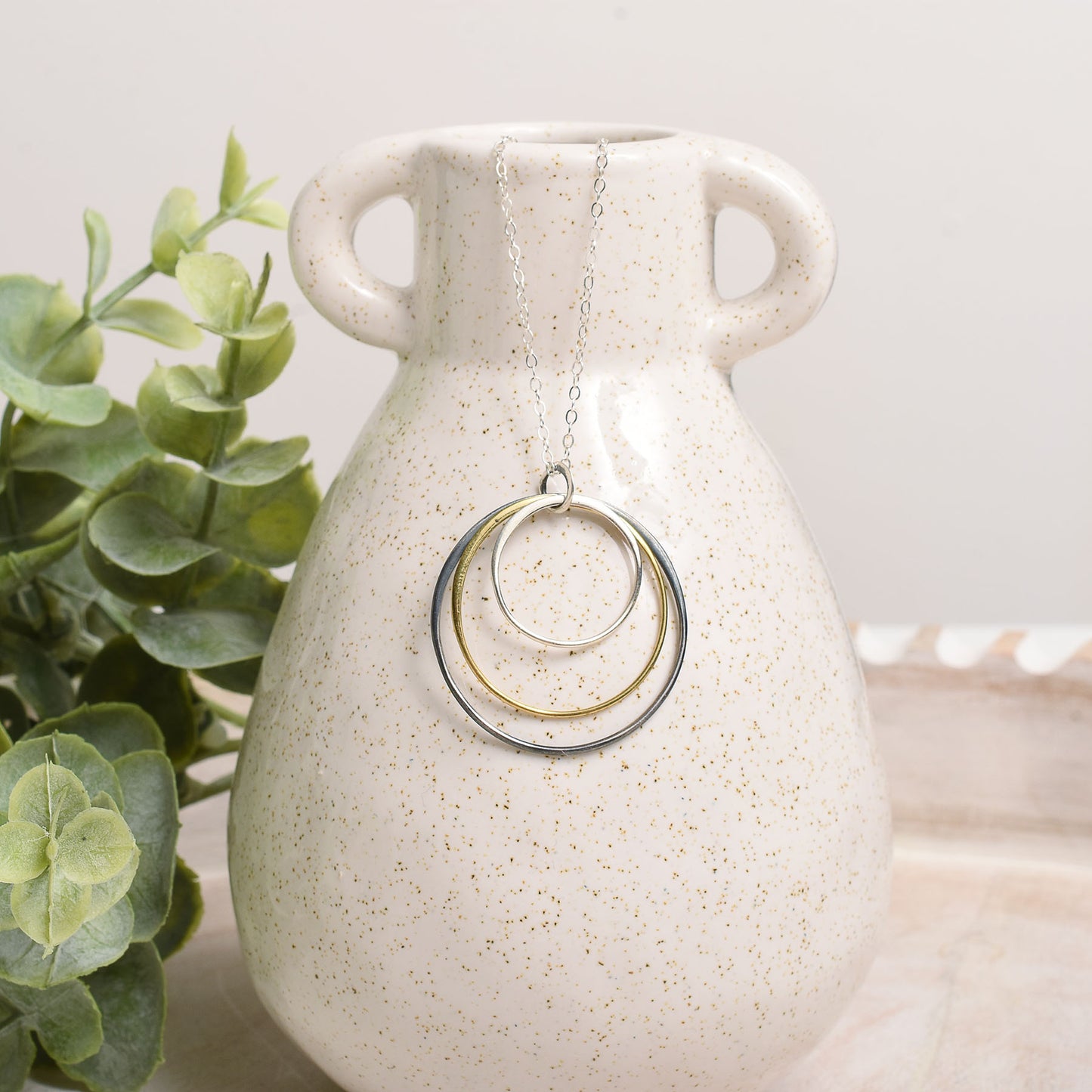Necklace with circular pendants on a white speckled vase next to a green plant