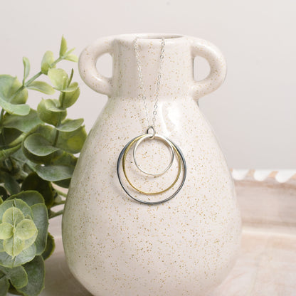 Necklace with circular pendants on a white speckled vase next to a green plant