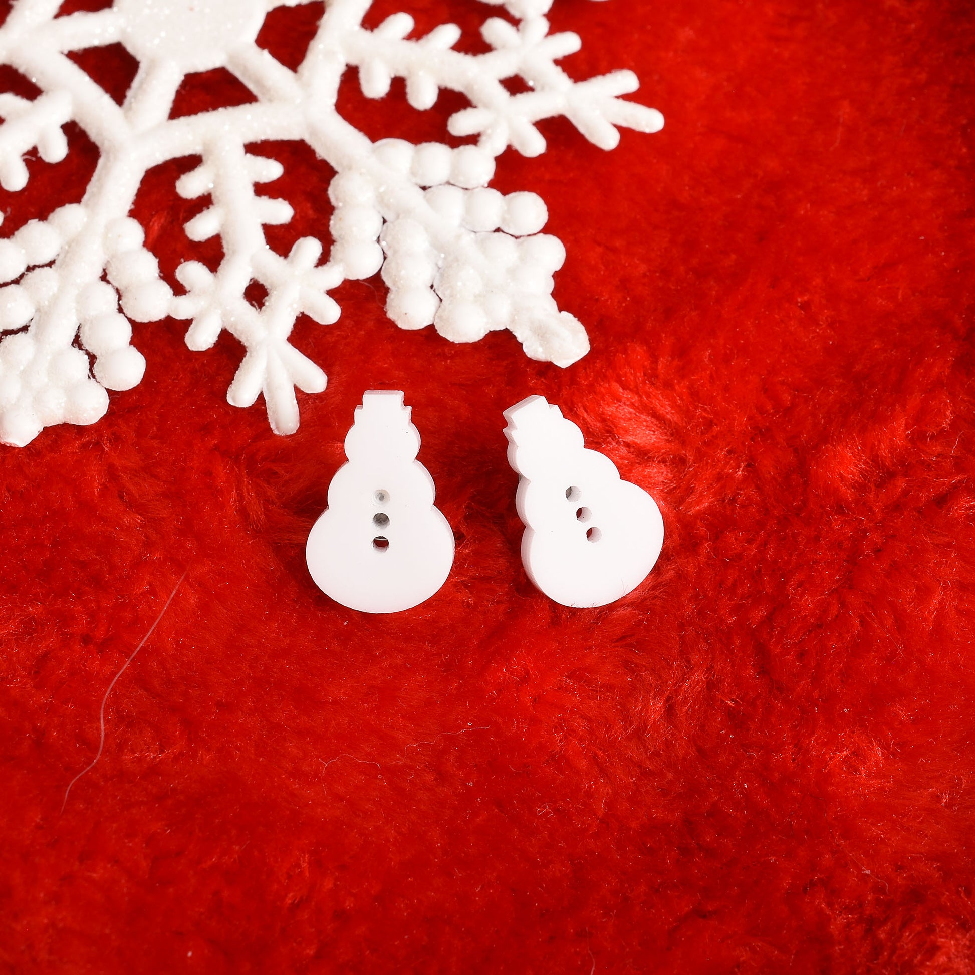 A pair of white snowman-shaped buttons with three buttons, displayed on a textured red background with a white decorative snowflake in the corner.